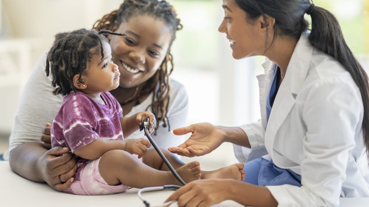A female doctor in a white lab coat sitting with a mother and her young son in a medical clinic.