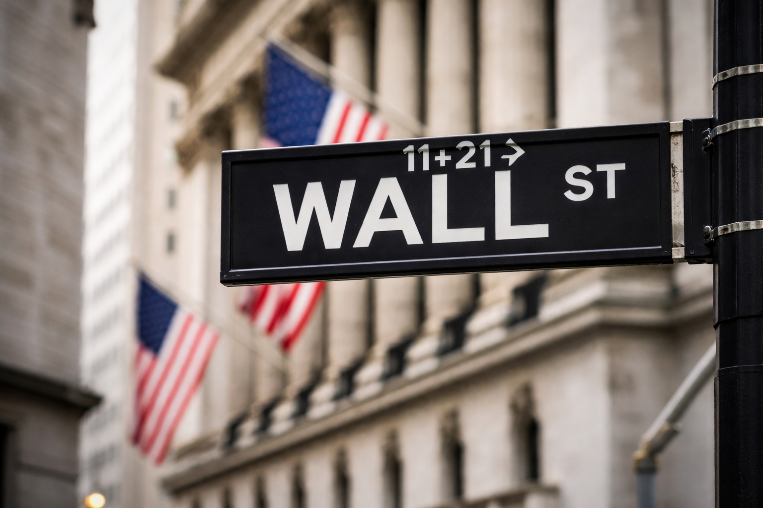 Wall Street street sign in New York with American flags and the New York Stock Exchange building in the background.